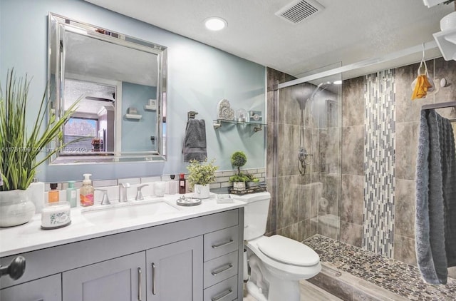 bathroom featuring vanity, toilet, a shower with shower door, and a textured ceiling