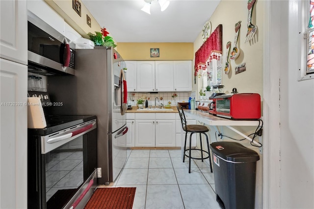 kitchen featuring white cabinetry, sink, backsplash, light tile patterned floors, and stainless steel appliances