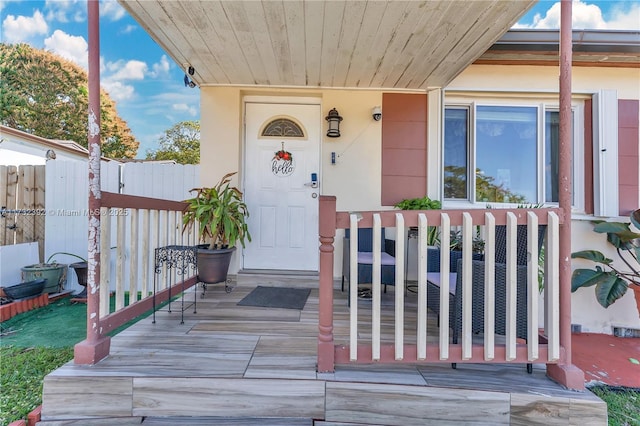 entrance to property with a porch, fence, and stucco siding