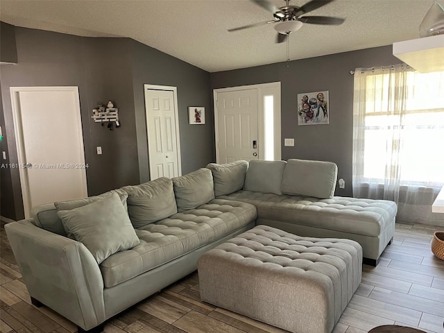 living room with ceiling fan, plenty of natural light, lofted ceiling, and a textured ceiling