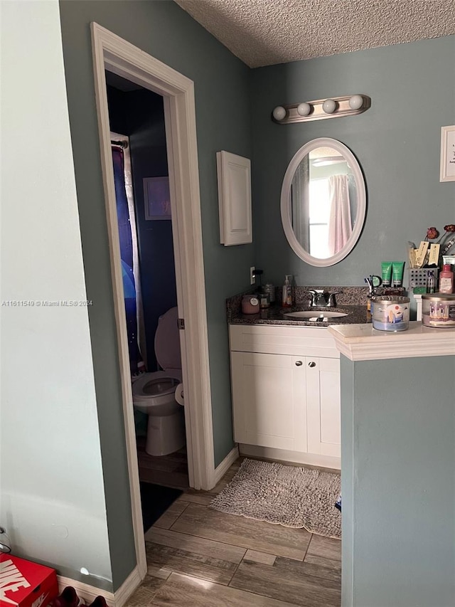 bathroom with hardwood / wood-style flooring, vanity, toilet, and a textured ceiling