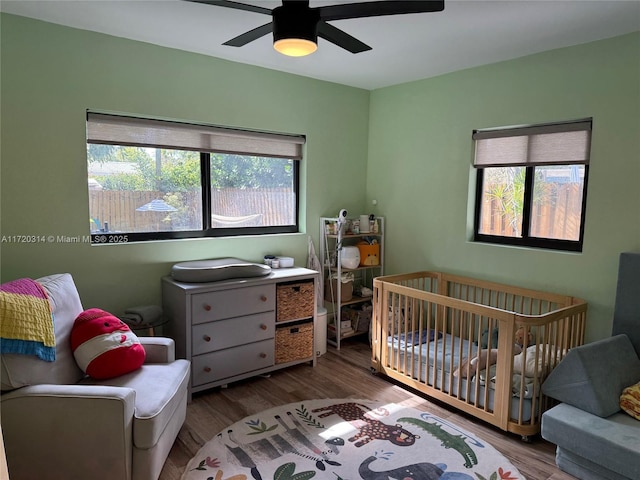 bedroom with multiple windows, a nursery area, ceiling fan, and light hardwood / wood-style flooring