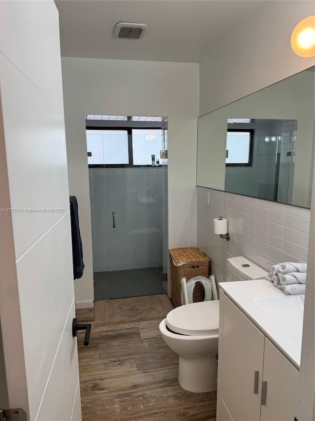 bathroom with hardwood / wood-style flooring, tile walls, an enclosed shower, vanity, and toilet