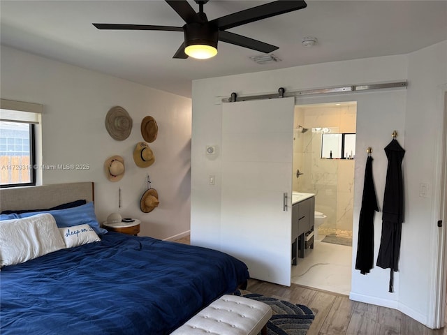 bedroom featuring ceiling fan, connected bathroom, a barn door, and light hardwood / wood-style flooring