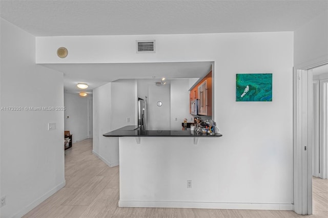 kitchen with a breakfast bar area, stainless steel appliances, light hardwood / wood-style floors, a textured ceiling, and kitchen peninsula