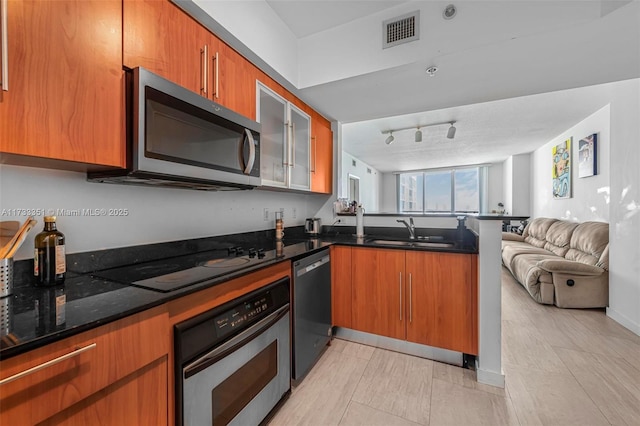 kitchen featuring sink, rail lighting, dark stone countertops, stainless steel appliances, and kitchen peninsula