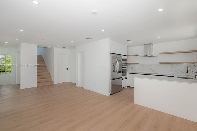 kitchen featuring stainless steel refrigerator with ice dispenser, wall chimney exhaust hood, sink, white cabinetry, and light wood-type flooring