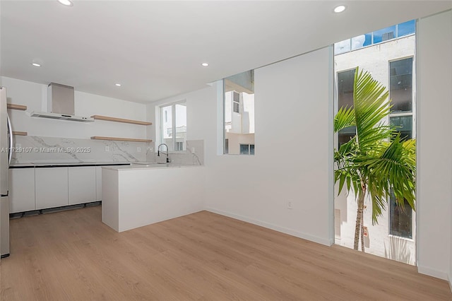 kitchen featuring light hardwood / wood-style flooring, white cabinetry, tasteful backsplash, kitchen peninsula, and wall chimney exhaust hood