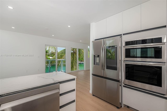 kitchen with light stone counters, appliances with stainless steel finishes, light hardwood / wood-style flooring, and white cabinets