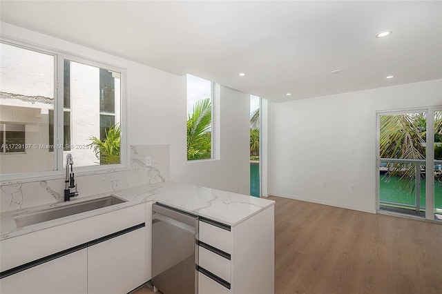 kitchen with sink, dishwasher, white cabinetry, light stone counters, and light hardwood / wood-style floors