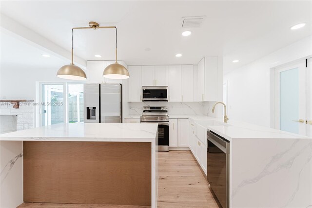 kitchen featuring decorative light fixtures, white cabinets, a center island, kitchen peninsula, and stainless steel appliances