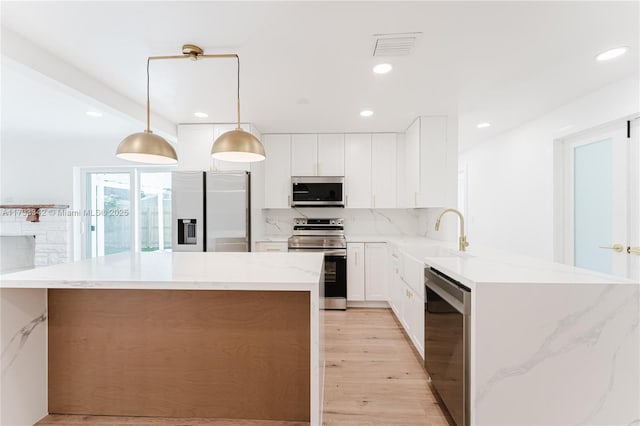 kitchen with sink, white cabinetry, decorative light fixtures, appliances with stainless steel finishes, and backsplash