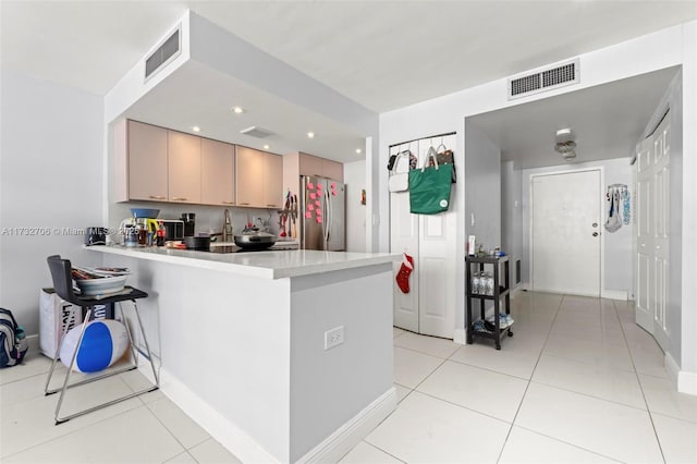 kitchen with stainless steel fridge, kitchen peninsula, light tile patterned floors, and light brown cabinets