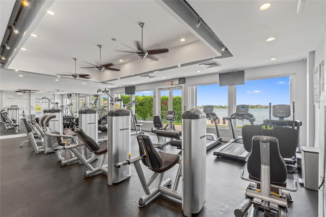 gym featuring recessed lighting, a ceiling fan, baseboards, visible vents, and a tray ceiling