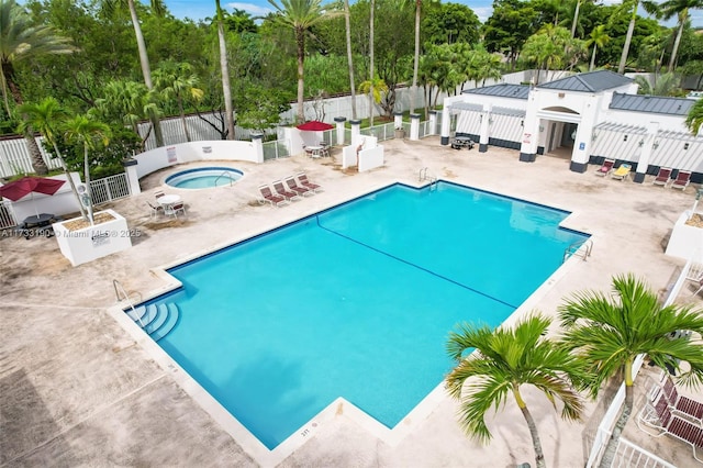 pool with fence, a hot tub, and a patio