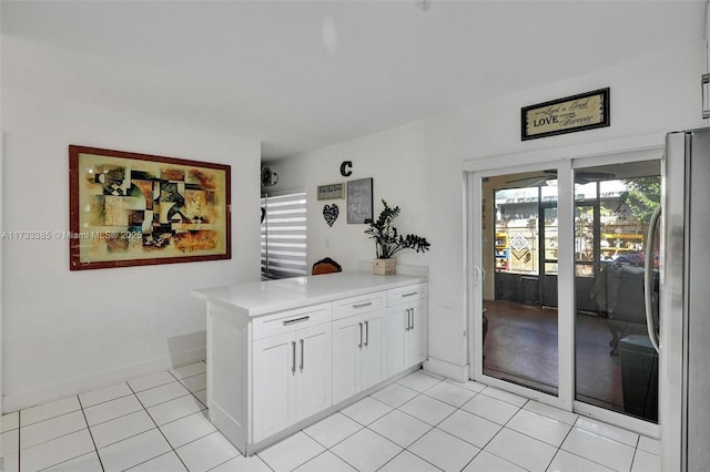 kitchen with light tile patterned floors, white cabinets, freestanding refrigerator, a peninsula, and light countertops