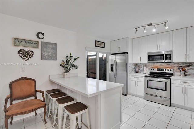 kitchen featuring stainless steel appliances, white cabinets, light countertops, and a breakfast bar area