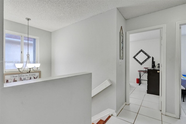 hall with light tile patterned floors, baseboards, a textured ceiling, an upstairs landing, and a notable chandelier