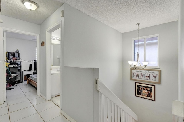 hall with light tile patterned flooring, a notable chandelier, a textured ceiling, and an upstairs landing