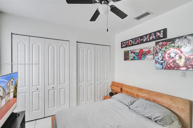 bedroom with a ceiling fan, light tile patterned flooring, visible vents, and two closets