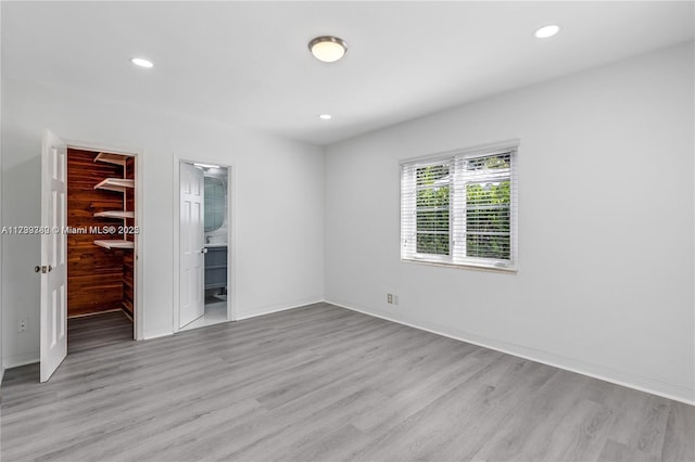 unfurnished bedroom featuring light hardwood / wood-style flooring, connected bathroom, a walk in closet, and a closet