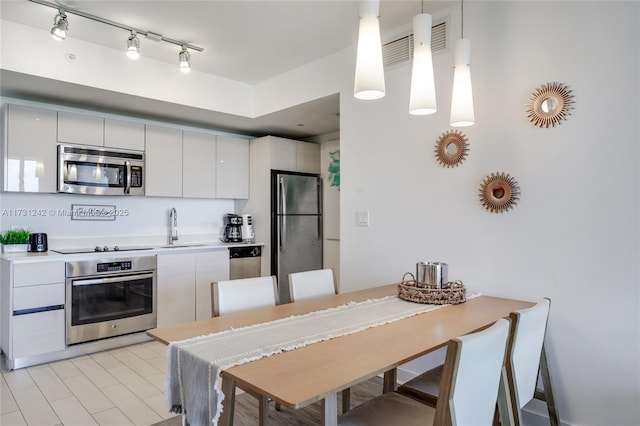 kitchen with stainless steel appliances, sink, white cabinets, and decorative light fixtures