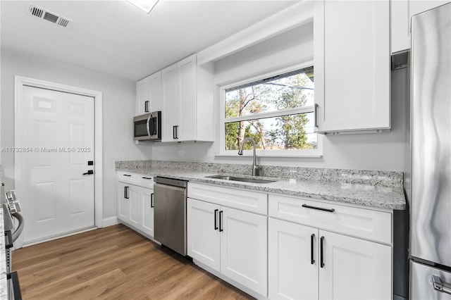 kitchen featuring sink, light wood-type flooring, appliances with stainless steel finishes, light stone countertops, and white cabinets