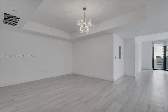 unfurnished room featuring a raised ceiling, a notable chandelier, and electric panel