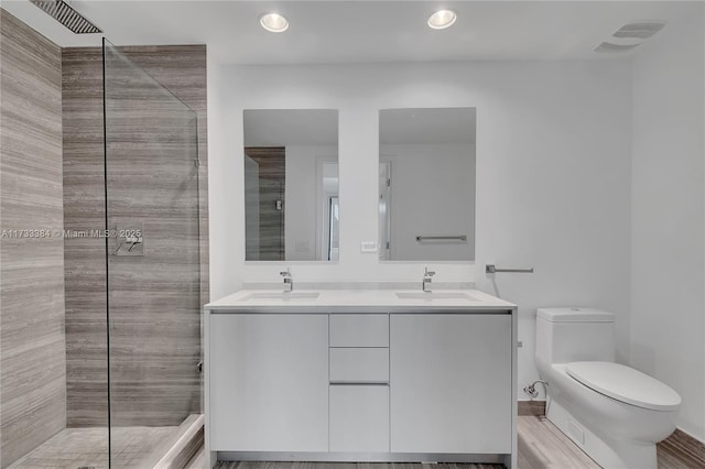 bathroom with tiled shower, vanity, toilet, and wood-type flooring