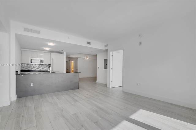 unfurnished living room featuring sink, electric panel, light wood-type flooring, and a notable chandelier