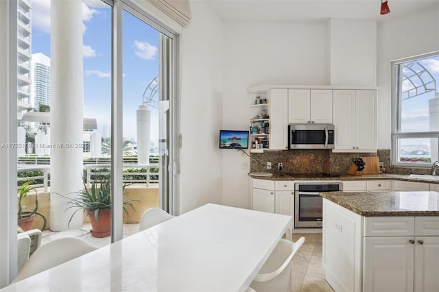 kitchen with white cabinetry, stainless steel appliances, dark stone counters, and a healthy amount of sunlight