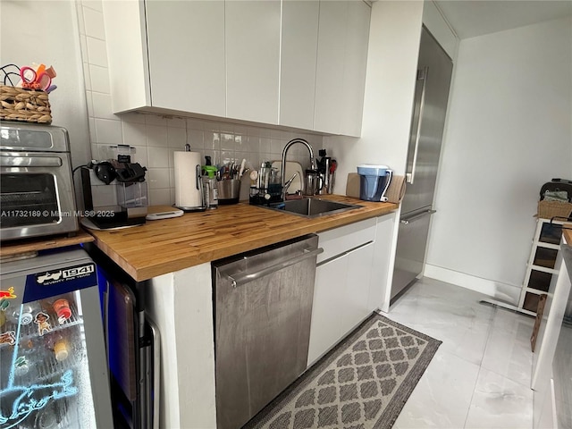 kitchen with butcher block countertops, tasteful backsplash, sink, white cabinets, and stainless steel dishwasher