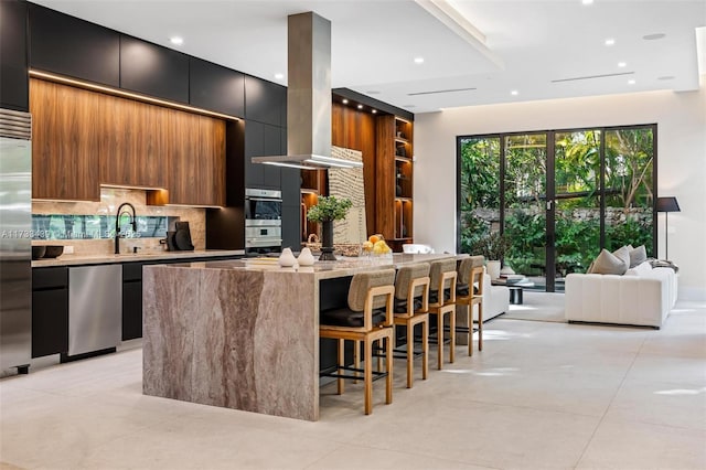 kitchen featuring sink, backsplash, a kitchen breakfast bar, a center island, and island range hood