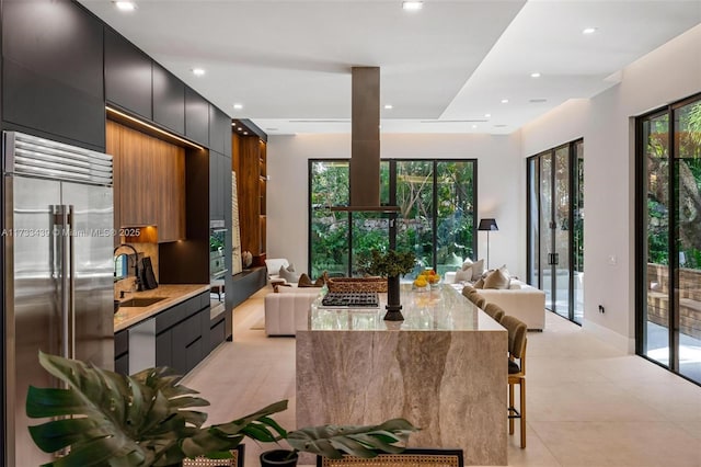 kitchen with sink, a breakfast bar area, light stone counters, built in fridge, and decorative backsplash