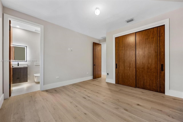 unfurnished bedroom with ensuite bath, light hardwood / wood-style floors, and a closet