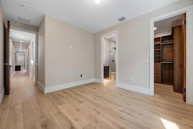 unfurnished bedroom with a closet, a spacious closet, ensuite bathroom, and light wood-type flooring