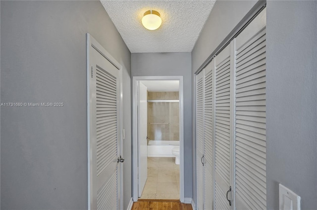 hall with a textured ceiling and light wood-type flooring