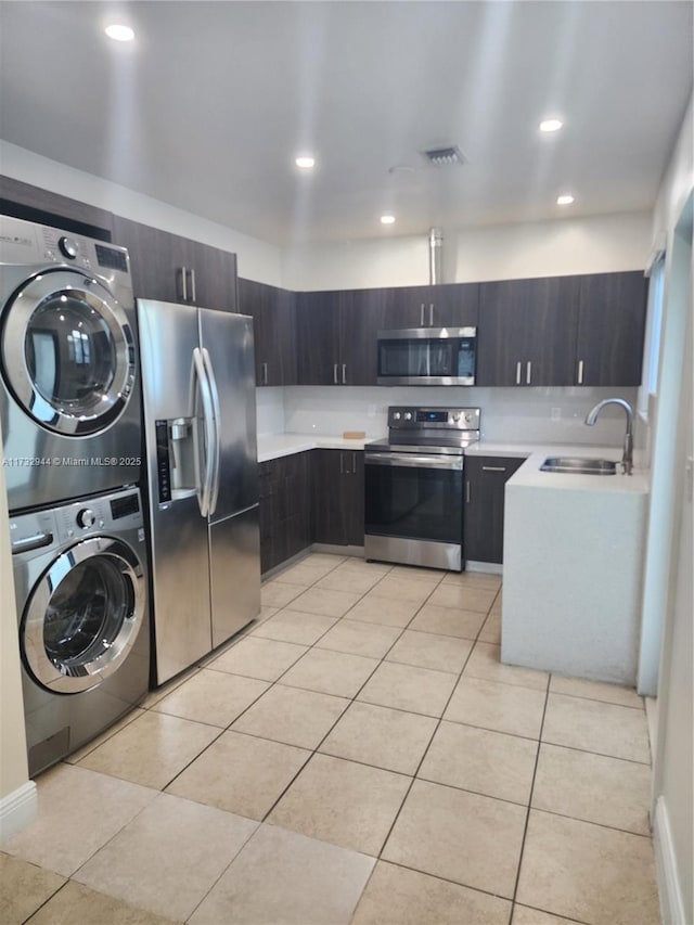 kitchen with stacked washer and dryer, sink, dark brown cabinets, light tile patterned floors, and appliances with stainless steel finishes