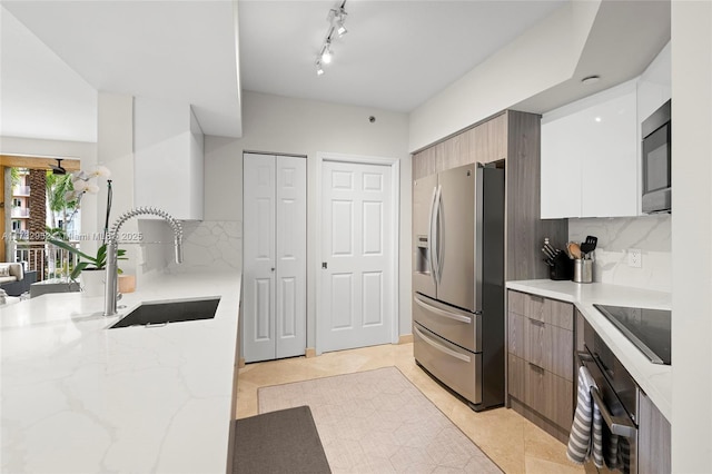 kitchen with light tile patterned flooring, tasteful backsplash, sink, light stone counters, and black appliances