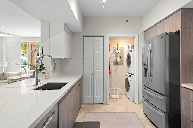 kitchen with tasteful backsplash, sink, stacked washer and dryer, stainless steel refrigerator with ice dispenser, and light stone countertops