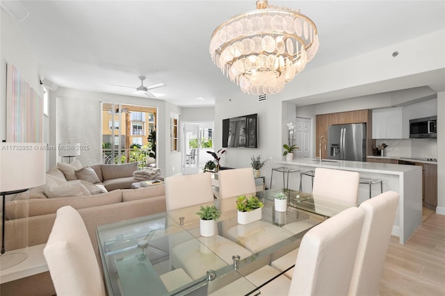 dining room featuring sink, ceiling fan with notable chandelier, and light hardwood / wood-style floors