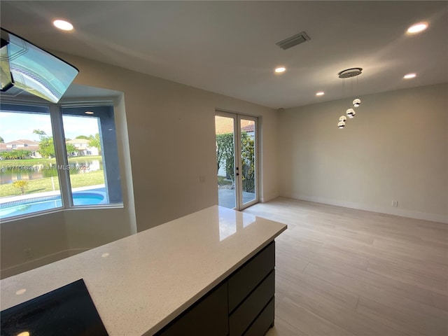 kitchen with light stone counters, hanging light fixtures, light hardwood / wood-style floors, and a water view