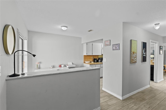 kitchen with white cabinetry, backsplash, a textured ceiling, and kitchen peninsula