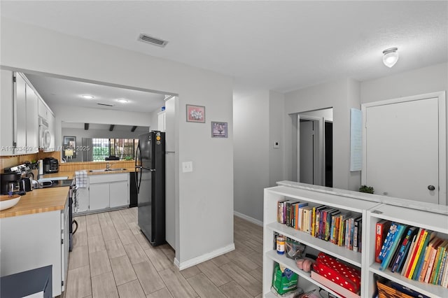 kitchen featuring stainless steel stove, sink, white cabinets, black fridge, and a textured ceiling