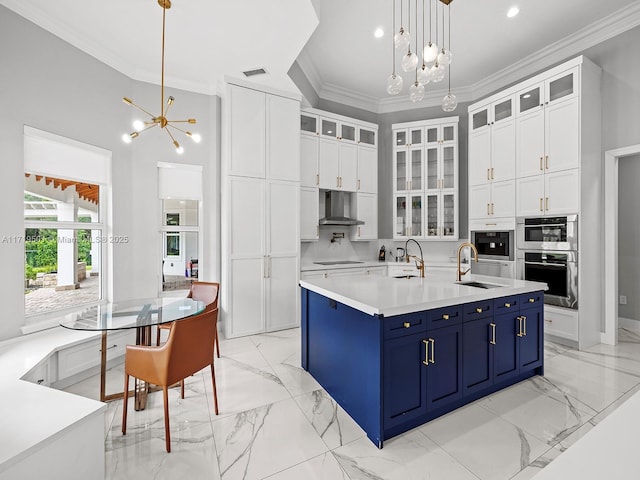 kitchen with an inviting chandelier, white cabinets, blue cabinetry, and wall chimney exhaust hood