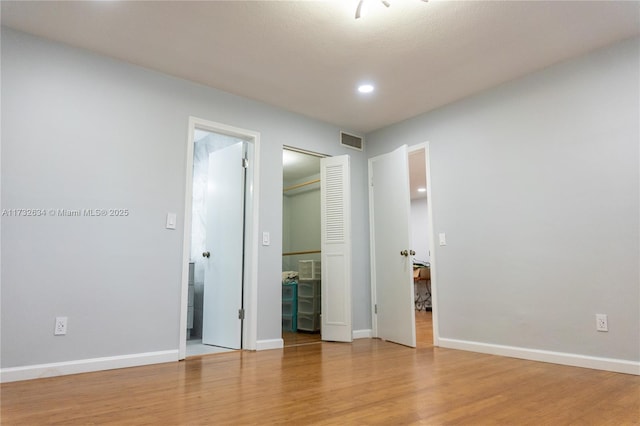 unfurnished bedroom with ensuite bath, a closet, and light wood-type flooring