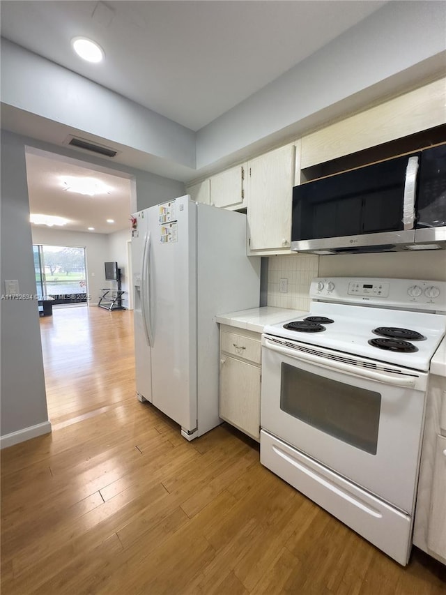 kitchen featuring white appliances, light hardwood / wood-style floors, decorative backsplash, and white cabinets