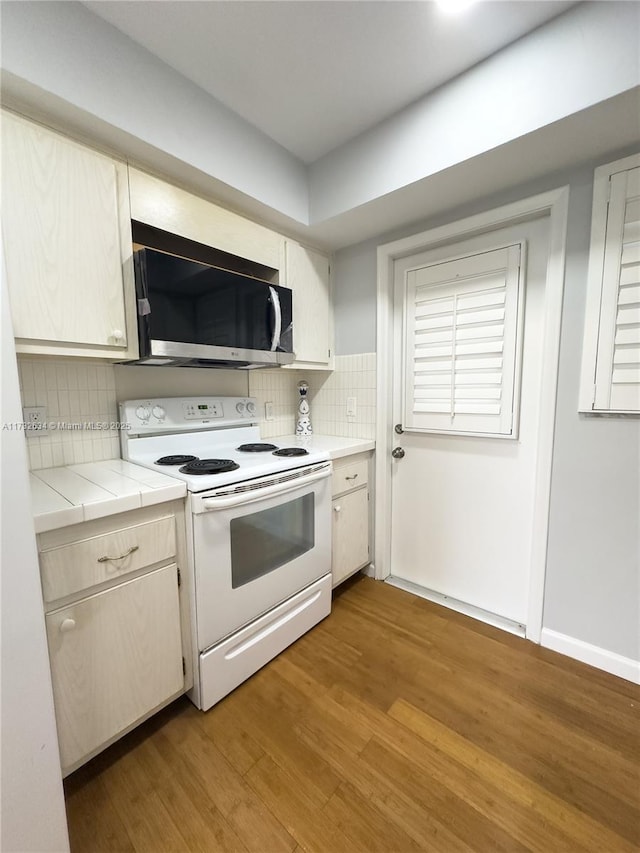 kitchen featuring white range with electric cooktop, tile counters, light hardwood / wood-style floors, and decorative backsplash