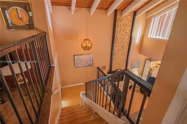 staircase featuring baseboards, a towering ceiling, wood ceiling, beamed ceiling, and wood finished floors