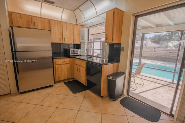 kitchen featuring black dishwasher, dark countertops, freestanding refrigerator, light tile patterned flooring, and a sink